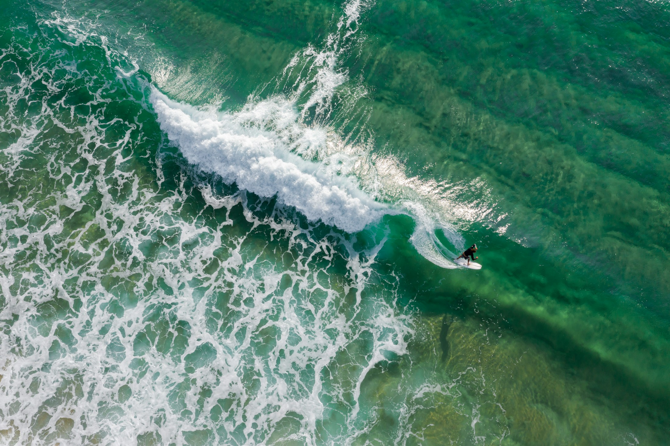 Un surfista traza su recorrido sobre una ola de agua turquesa